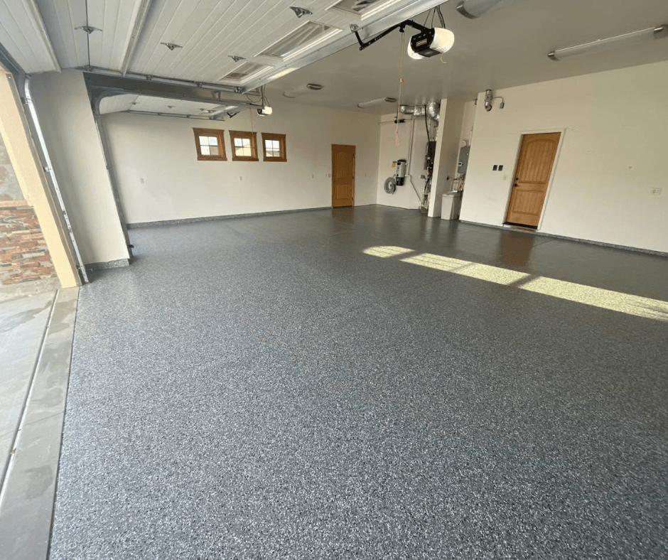 Empty two-car garage with epoxy speckled floor, white walls, and a wooden door; garage door opener overhead and small windows on the far wall