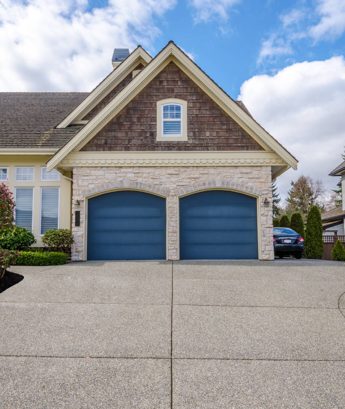 Front view of a two-car garage with blue doors, stone façade, and a peaked roof on a suburban house