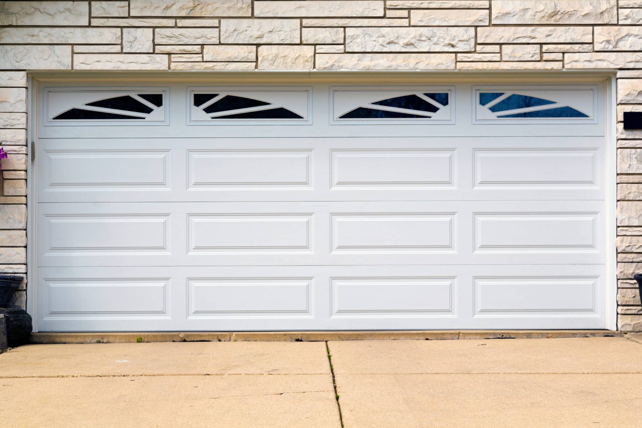 White sectional garage door with decorative angled window panes and a stone veneer facade above it, on a concrete driveway.