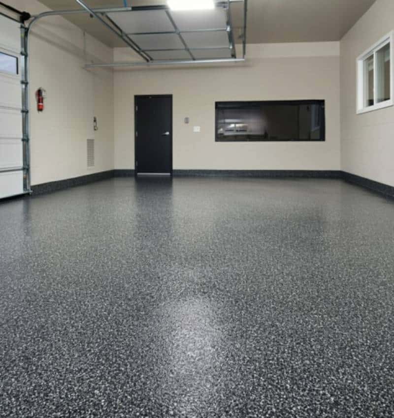Empty, clean garage with a speckled gray epoxy floor, a dark entry door, a windowed wall, and a left-side garage door.
