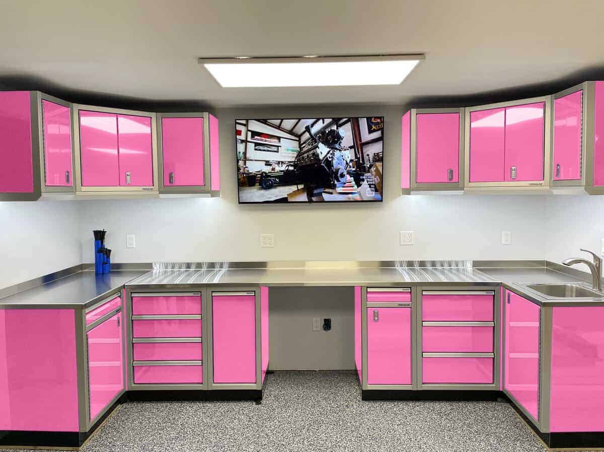 Bright pink and stainless steel workshop kitchenette with upper and lower cabinets and a wall-mounted TV in the center. (Informative)